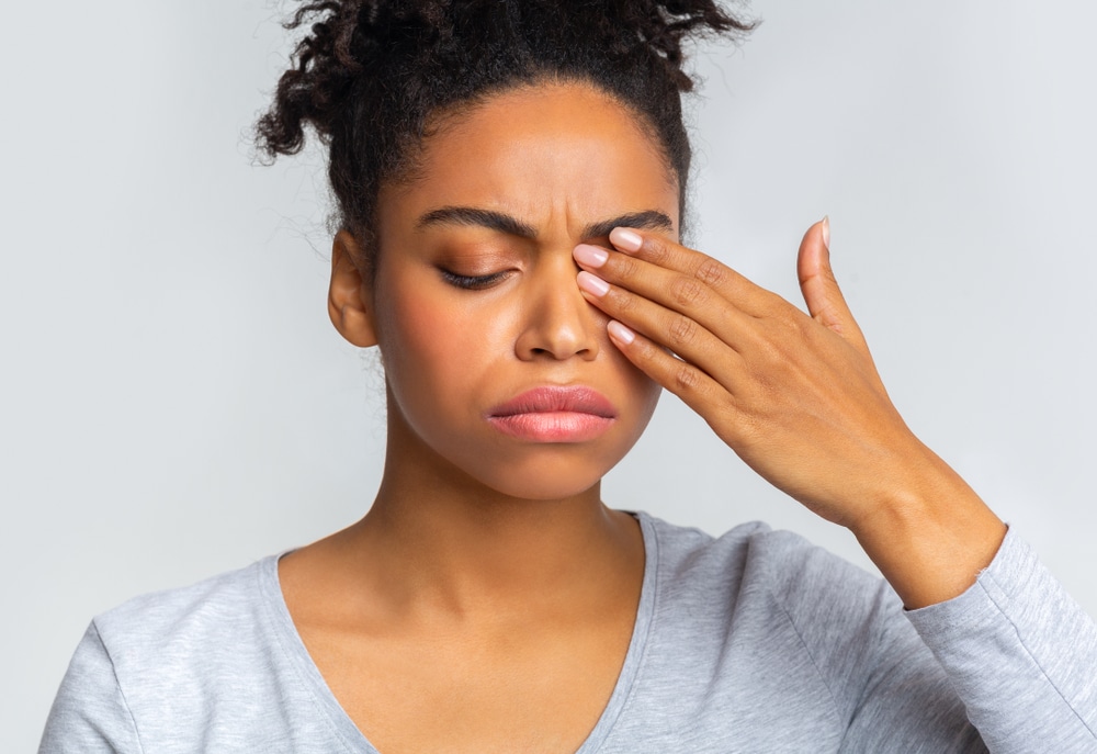 Young woman frowning and rubbing her eye, experiencing an eye twitch or blepharospasm, in need of treatment.